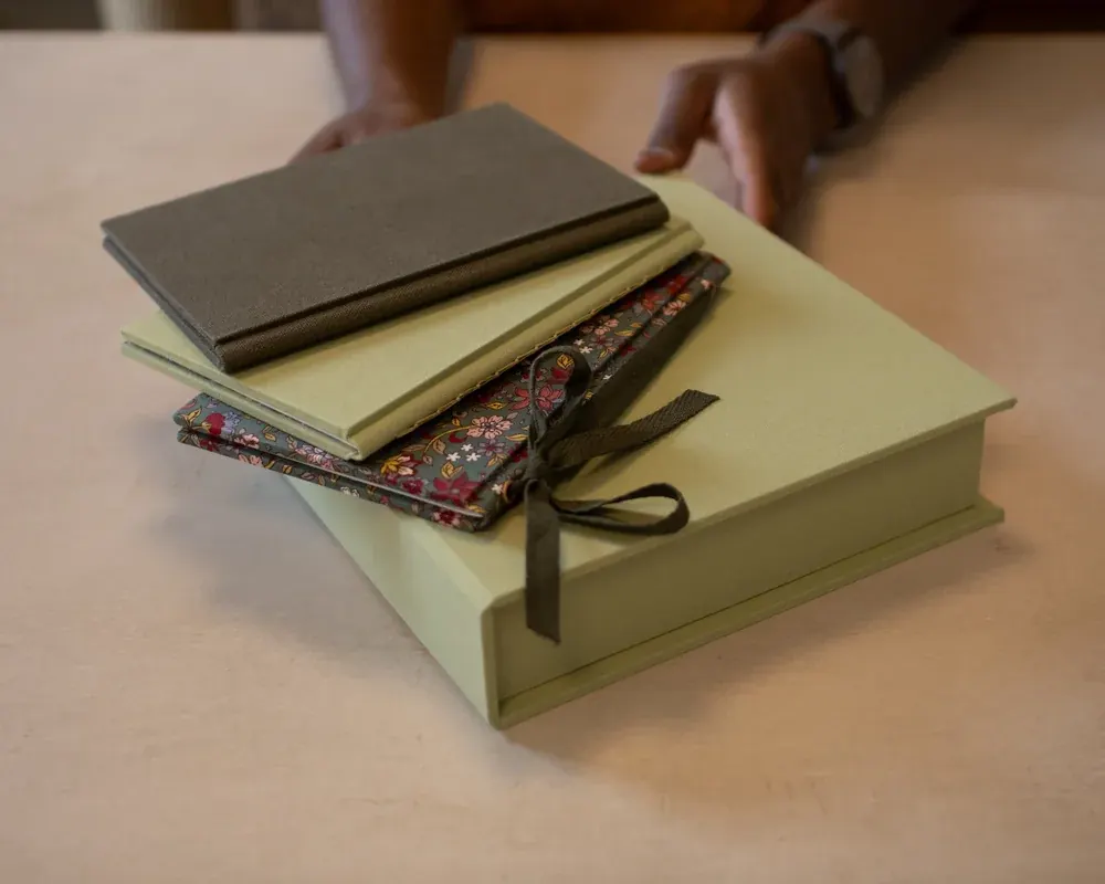 Stack of wrapped gifts and notebooks on a beige table with a person in the background.